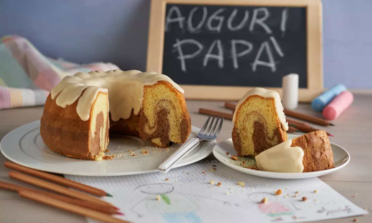Ciambella variegata al cacao con glassa chiara colata sui bordi, servita su piatti bianchi e decorata da disegni infantili e gessetti colorati